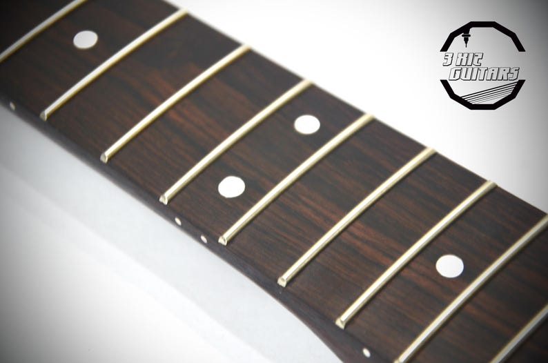 May include: Close-up of a guitar fretboard with dark brown wood and white fret markers. The frets are thin, light-colored metal. The logo "3 Kit Guitars" is in the upper right corner.