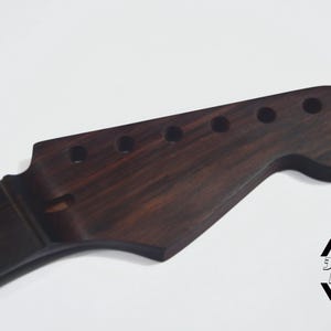 May include: A dark brown guitar neck with a headstock featuring six tuning peg holes. The neck has a fretboard with white inlays. The logo "3 Hitz Guitars" is visible in the bottom right corner.