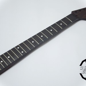 May include: A dark brown guitar neck with white fret markers. The neck has a headstock with tuning peg holes. The logo for 3 Kit Guitars is in the lower right corner. The neck is made of wood.