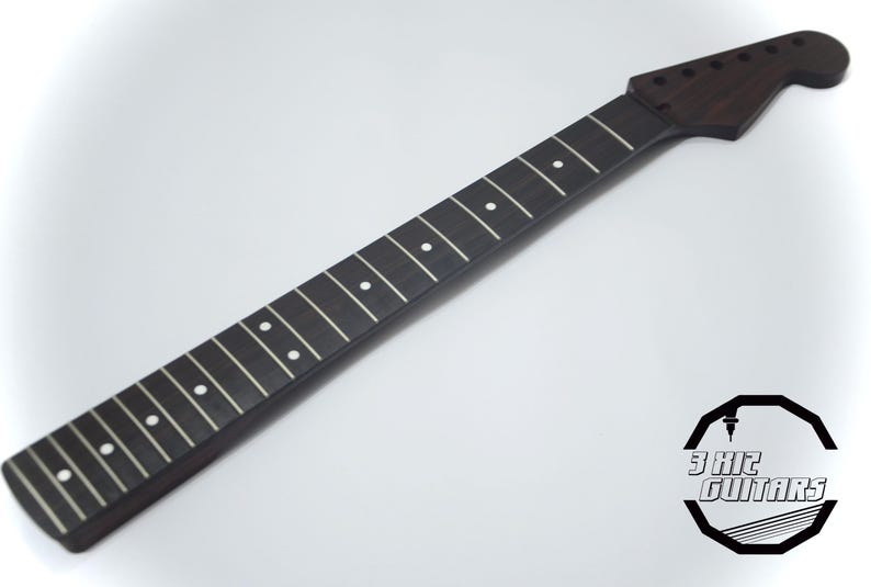 May include: A dark brown guitar neck with white fret markers. The neck has a headstock with tuning peg holes. The logo for 3 Kit Guitars is in the lower right corner. The neck is made of wood.