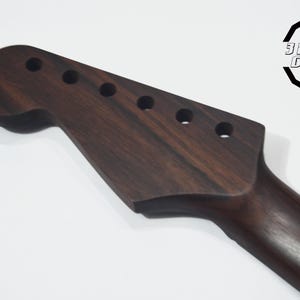 May include: A dark brown guitar neck with tuning peg holes. The headstock has a rounded shape, and the neck tapers down. The logo "3 Hit Guitars" is in the upper right corner.