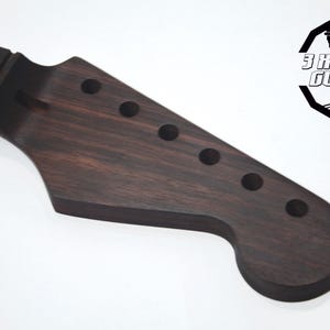 May include: A dark brown guitar neck with six tuning peg holes. The neck is made of wood and has a smooth finish. The logo for "3 Kit Guitars" is in the upper right corner.