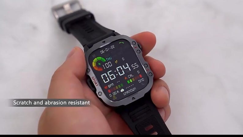 May include: A black smartwatch with a gray bezel and black band displays the time, date, and health metrics. The screen shows "06:04 55" and "100". The watch is held in a hand, and the text "Scratch and abrasion resistant" is visible.
