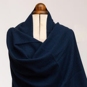 Peut inclure: Un châle bleu marine drapé sur un mannequin en bois. Le tissu est de couleur unie et semble doux. Le châle est plié pour créer un effet de superposition, mettant en valeur la texture et le drapé du matériau. Le fond est blanc uni.