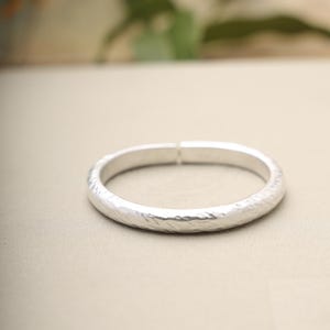 May include: A silver-colored bracelet with a hammered texture. The bracelet is a simple, circular design, and the surface has a slightly uneven, textured appearance. The bracelet is shown on a neutral background.