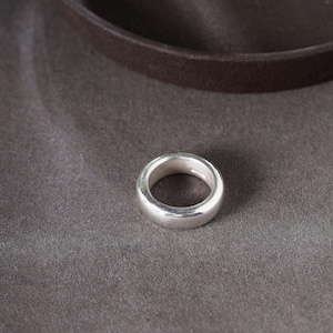 May include: A silver ring with a smooth, rounded design. The ring is made of a shiny, metallic material and sits on a gray surface. The ring's simple, classic style makes it suitable for everyday wear.