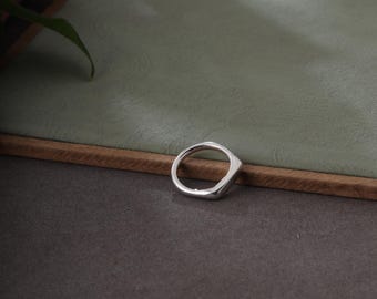 May include: A silver ring with a geometric design. The ring has a smooth, polished finish and a slightly angular shape. The ring is set against a neutral background.