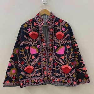 Peut inclure: Veste brodée bleu marine avec un motif floral dans les tons de rose, de rouge et d'or. La veste a un col montant et est doublée d'un tissu rayé. La veste est suspendue à un cintre en bois.