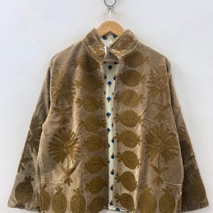 May include: A brown velvet jacket with intricate embroidered floral and fruit designs. The jacket has a high collar and long sleeves. The interior lining features a white fabric with a blue floral pattern. The jacket is hanging on a wooden hanger.