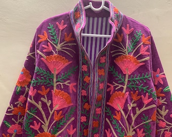 May include: A purple velvet jacket with intricate floral embroidery in shades of pink, orange, and green. The jacket features a mandarin collar and is lined with a striped fabric. The embroidery includes flowers and leaves.