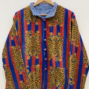 Op de afbeelding: Omkeerbare jas met tijgerprint. De jas heeft een rood, blauw en geel kleurenschema met een streepjespatroon op de kraag en een tijgerpatroon op de body. Het heeft een knoopsluiting en twee zakken.