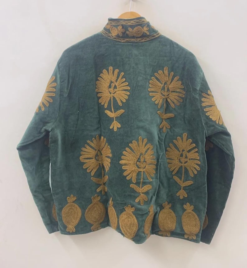 May include: A teal jacket with intricate gold floral embroidery. The jacket features a high collar and long sleeves. The floral design is repeated across the front and back of the jacket, creating a decorative pattern. The jacket is hanging on a wooden hanger.