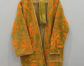 May include: A long, olive green robe with vibrant orange floral embroidery. The robe features a shawl collar, two front pockets, and a matching belt. The interior lining has a striped pattern. The robe is hanging on a wooden hanger.
