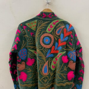 May include: A dark green jacket with colourful embroidered floral and paisley designs. The jacket features pink, blue, orange, and green accents, with a brown embroidered outline. The jacket is hanging on a wooden hanger.