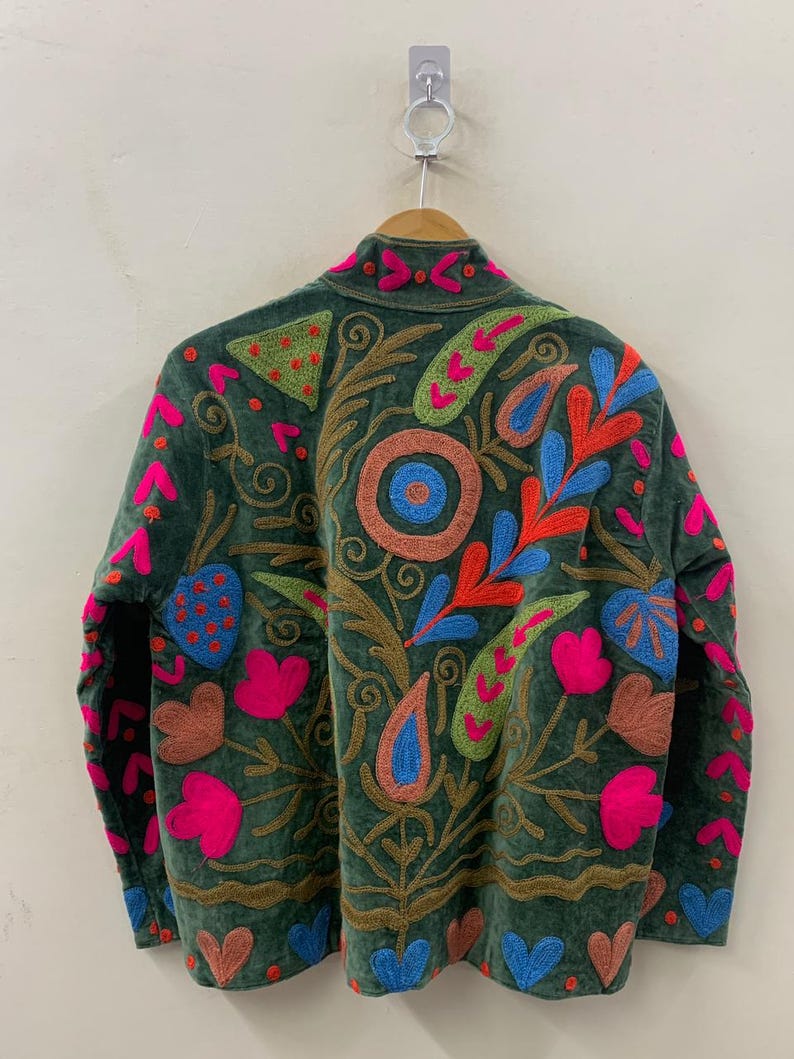 May include: A dark green jacket with colourful embroidered floral and paisley designs. The jacket features pink, blue, orange, and green accents, with a brown embroidered outline. The jacket is hanging on a wooden hanger.