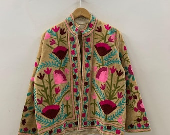 May include: A tan jacket adorned with colourful floral embroidery in pink, burgundy, and teal. The jacket has a mandarin collar and a striped lining, displaying a bohemian aesthetic.