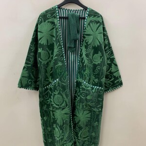 May include: An emerald green robe with detailed floral embroidery. The robe has two front pockets and a striped interior lining. The edges are trimmed with a white and green striped pattern. The robe is hanging on a black hanger.