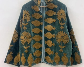 Puede incluir: Chaqueta verde oscuro con diseños florales y ovalados bordados en color dorado. La chaqueta tiene cuello mandarín y forro a rayas. La chaqueta está colgada en una percha de madera sobre un fondo blanco.