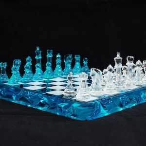 Op de afbeelding: Een compleet schaakspel met een blauw en wit schaakbord. De schaakstukken zijn transparant, met de stukken aan de ene kant lichtblauw en de andere kant helder. Het bord heeft een blauwe rand.