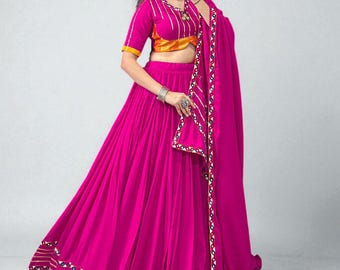 May include: A vibrant fuchsia-colored skirt and top set. The top is a cropped style with a yellow and gold accent. The skirt is a full, flowing design. The set includes a matching fuchsia scarf with gold and white trim. The outfit is suitable for festive occasions.