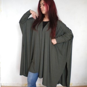 Peut inclure: Une tunique longue et ample de couleur olive avec des manches longues et un col rond haut. La tunique a une fente latérale et est portée avec un jean bleu.