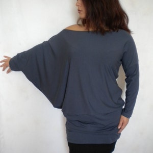 May include: A loose-fitting, long-sleeved, gray tunic top with a slightly off-the-shoulder neckline. The top is made of a soft, drapey fabric and has a relaxed fit.