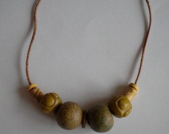 Puede incluir: Un collar de cordón de cuero marrón con cinco cuentas verdes y amarillas. Las cuentas son redondas y tienen una superficie texturizada.