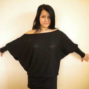 May include: A woman wearing a black off-the-shoulder top with long sleeves. The top is loose fitting and has a draped look.