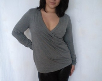 Puede incluir: Una camisa gris de manga larga con cuello en V profundo y estilo de envoltura. La camisa se lleva con leggings negros.