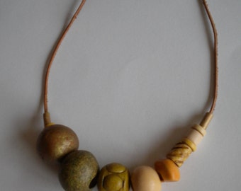 Puede incluir: Un collar de cuero marrón con cinco cuentas de madera. Las cuentas son en tonos de marrón, verde y amarillo.