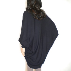 May include: A black, long-sleeved, oversized sweater with a draped, asymmetrical design. The sweater is made of a soft, knit fabric.