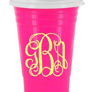 Op de afbeelding: Een felroze plastic beker met een wit deksel. De beker heeft een geel monogramontwerp. De beker is ontworpen voor drankjes. De beker is gemaakt van plastic.
