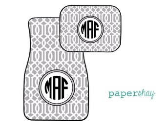 May include: A set of two gray car floor mats with a white geometric pattern and a black monogram "MAF" in the center of each mat.