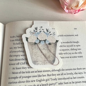 May include: A white wicker basket filled with white and blue hydrangea flowers. The basket is sitting on a page of a book with text about a beach party.
