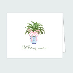 May include: A green plant with a pink bow tied around the stem, in a blue and white patterned pot. The text "Bethany Lions" is written below the pot.