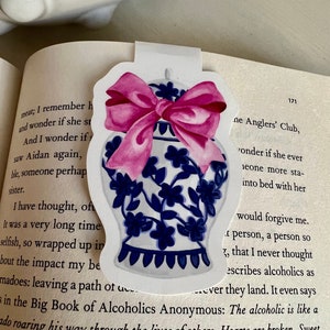 May include: A white ceramic ginger jar with a blue and white floral design and a pink bow. The jar is on a white background. The text "The alcoholic is like a..." is visible in the background.