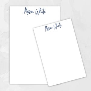 May include: Two white notepads with blue ink, one larger than the other, both with the name "Mason White" written on them.