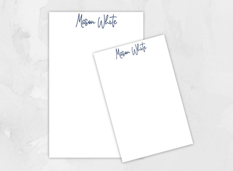 May include: Two white notepads with blue ink, one larger than the other, both with the name "Mason White" written on them.