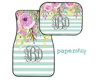 May include: A set of two car floor mats with a light blue and white striped pattern. The mats feature a watercolor floral design with pink, purple, and yellow flowers. The mats are personalized with a monogram in the center.