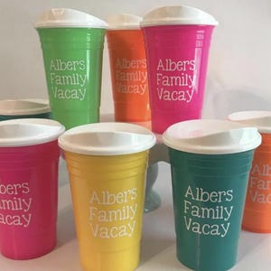 Op de afbeelding: Een verzameling kleurrijke plastic bekers met witte deksels. De bekers zijn in verschillende tinten, waaronder groen, oranje, roze, geel en teal. Elke beker is bedrukt met de witte tekst "Albers Family Vacay". Perfect voor een picknick.