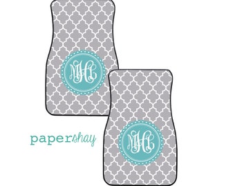May include: Two gray car floor mats with a white geometric pattern. Each mat has a turquoise circle with white monogram initials "MJC" in the center.