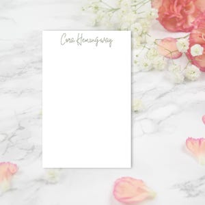 May include: A white notepad with the name "Cora Hemingway" written in cursive at the top.
