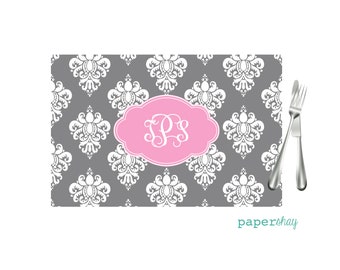 May include: Gray and white damask patterned placemat with a pink oval monogram that says "SPS".
