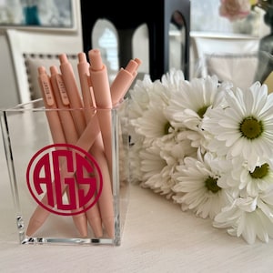May include: A clear acrylic desk organizer with a pink monogram "AGS" on the front. The organizer is filled with pink pens that say "U-Right" on the side.