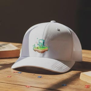 Könnte beinhalten: Weiße Trucker-Cap mit Mesh-Rückseite und gebogenem Schirm. Auf der Vorderseite befindet sich eine Cartoon-Grafik eines grünen Videospielkonsolen-Charakters auf einem kleinen Stück Land mit Blumen.