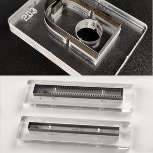 Pu&ograve; includere: Modelli in acrilico trasparente con inserti metallici. Un modello ha il numero "203" inciso sulla superficie. Di seguito sono mostrati due modelli aggiuntivi, ciascuno con un inserto metallico. I modelli sono su uno sfondo bianco e nero.