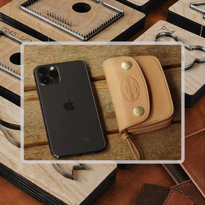 Pu&ograve; includere: Uno smartphone nero e un portachiavi in pelle marrone chiaro con chiusure a scatto in ottone sono esposti su una superficie di legno. Il portachiavi ha un bordo cucito e un piccolo anello in pelle. Vari strumenti artigianali in legno sono sullo sfondo.
