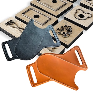 Op de afbeelding: Twee lederen ambachtelijke projecten, één in grijs en één in oranje, worden getoond voor verschillende houten stansgereedschappen. Het grijze leren stuk is gestikt met een gebogen ontwerp. Het oranje leren stuk is gestikt met een vergelijkbaar ontwerp.