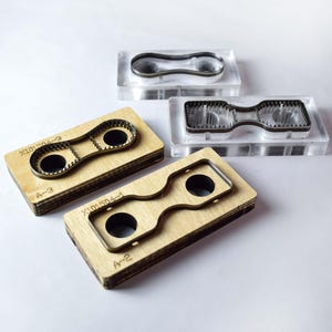Pu&ograve; includere: Quattro fustelle per l'artigianato. Due sono inserite in blocchi di acrilico trasparente e due in blocchi di legno. Ogni strumento ha una forma unica con un design centrale e un contorno metallico. I blocchi di legno presentano le marcature "X101504-3", "A-3", "X101504-1" e "A-2".