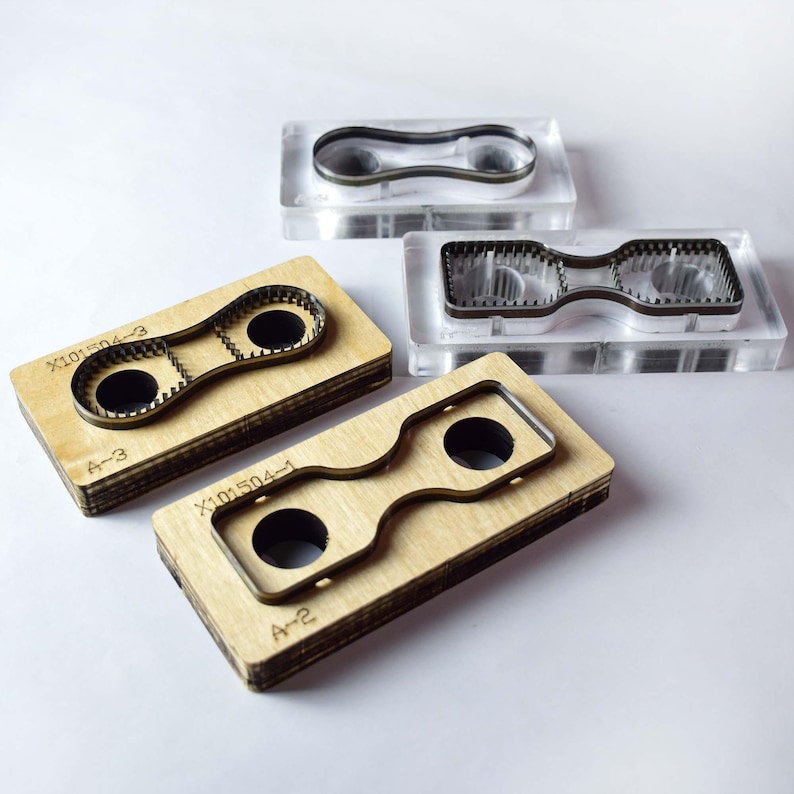 Pu&ograve; includere: Quattro fustelle per l'artigianato. Due sono inserite in blocchi di acrilico trasparente e due in blocchi di legno. Ogni strumento ha una forma unica con un design centrale e un contorno metallico. I blocchi di legno presentano le marcature "X101504-3", "A-3", "X101504-1" e "A-2".